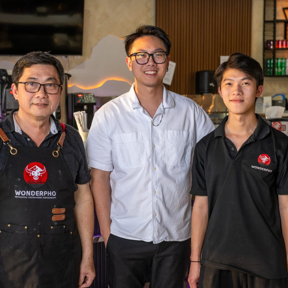 Three smiling men, likely owners or staff, standing together inside the WonderPho restaurant.