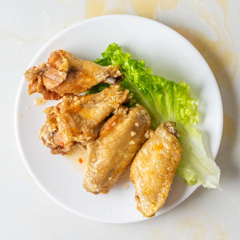 Four golden-brown chicken wings with garlic and sauce, garnished with fresh green lettuce on a white plate.